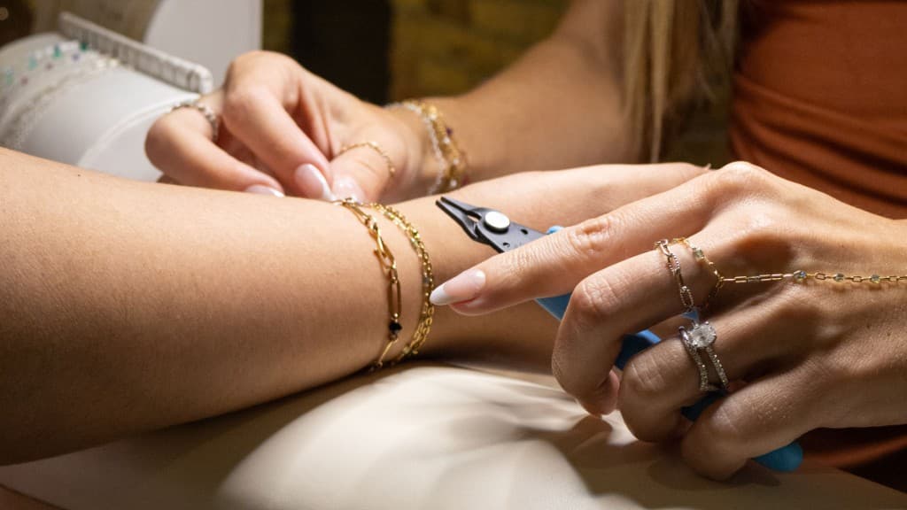 Close-up of hands fitting a gold permanent bracelet with jewelry pliers