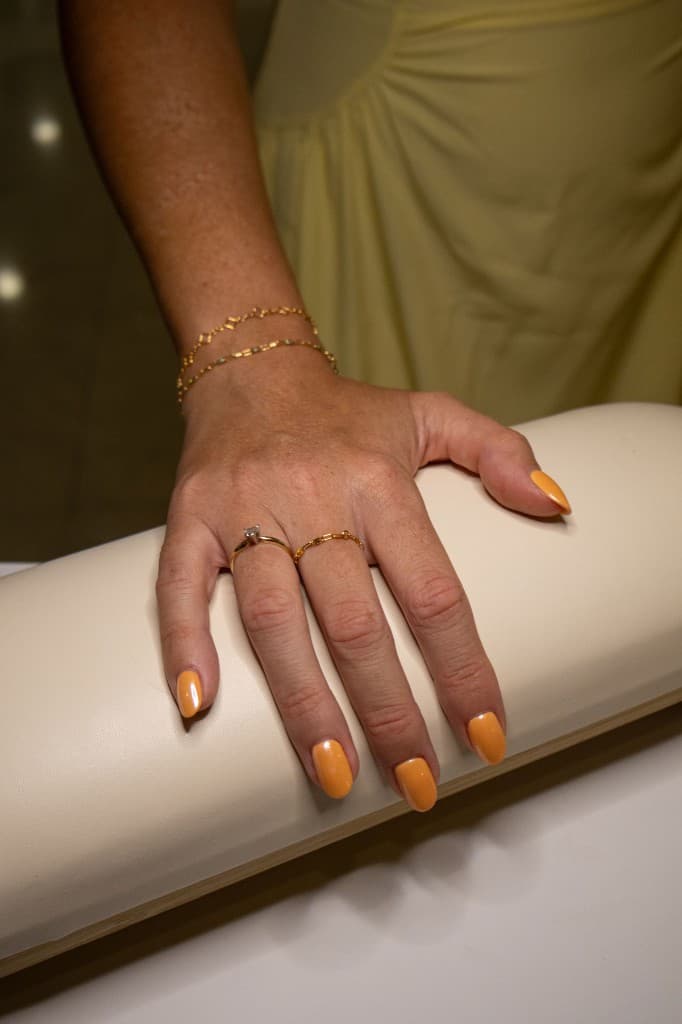 Close-up of a hand with gold chain bracelets and rings resting on a padded fitting armrest