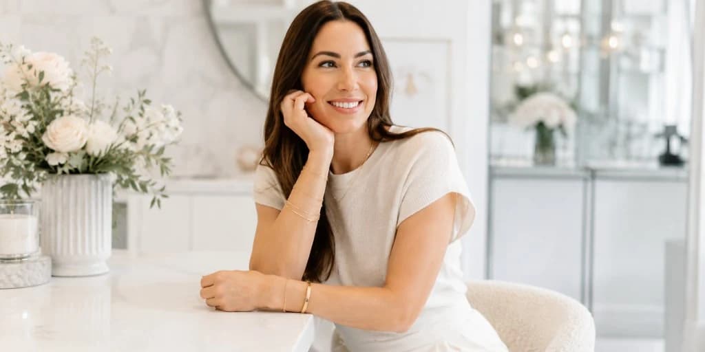 Woman smiling at a marble table wearing gold permanent jewelry